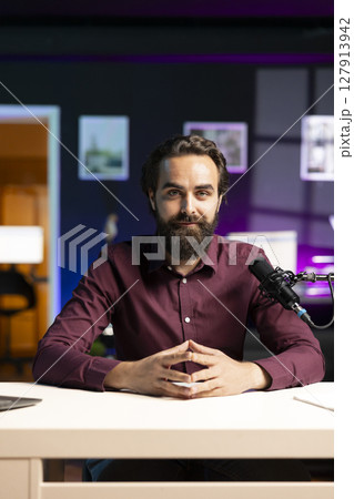 Portrait of influencer in home studio using professional microphone to record live broadcast for online streaming platforms, talking with fans. Smiling media star hosts q and a session with viewers Portrait of influencer in home studio using professional microphone to record live broadcast for online streaming platforms, talking with fans. Smiling media star hosts q and a session with viewers 127913942