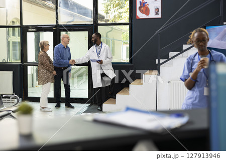 Old male patient receives treatment plan recommendations from black doctor during appointment in the lobby, discussing wellness strategies and prevention methods in a modern clinic. 127913946