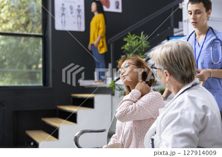 Doctor consulting patient about neck pain symptoms during medical appointment at hospital lobby. Healthcare staff discussing treatment plan and posture adjustments to relieve muscle strain. 127914009