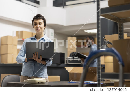 Woman employee working in a warehouse on order processing in small business depot, preparing taped boxes for local brand express delivery logistics. Distribution center supply room. 127914043