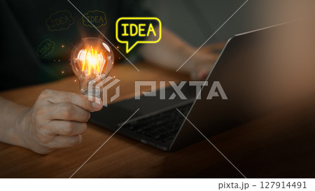 Male hand holding a glowing light bulb and "idea" text bubbles, symbolizing creative ideas and innovation, while the person works on a laptop, representing brainstorming and technology. Male hand holding a glowing light bulb and "idea" text bubbles, symbolizing creative ideas and innovation, while the person works on a laptop, representing brainstorming and technology. 127914491