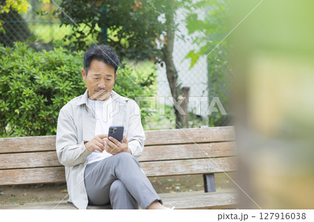 公園のベンチでスマホを見るシニア男性 公園のベンチでスマホを見るシニア男性 127916038