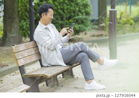 公園のベンチでスマホを見るシニア男性 公園のベンチでスマホを見るシニア男性 127916044