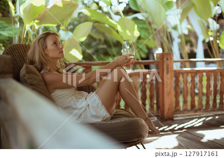 Young woman sit on open-air veranda of wooden bungalow with tropical garden view. Girl relaxing in luxury villa on family summer vacation. Tropical lifestyle. Young woman sit on open-air veranda of wooden bungalow with tropical garden view. Girl relaxing in luxury villa on family summer vacation. Tropical lifestyle. 127917161