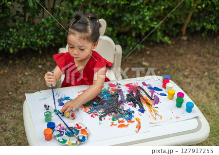 happy toddler girl painting watercolor in paper at backyard. happy toddler girl painting watercolor in paper at backyard. 127917255