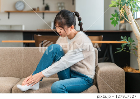 自宅のソファに座り足首を抑える小学生,中学生の女の子 自宅のソファに座り足首を抑える小学生,中学生の女の子 127917527