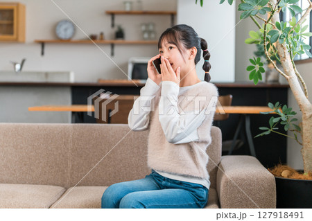 自宅のソファに座りスマホで通話する小学生,中学生の女の子 自宅のソファに座りスマホで通話する小学生,中学生の女の子 127918491