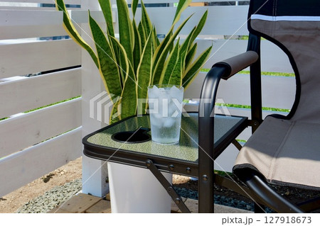 白いウッドフエンスをバックに椅子のサイドテーブルに置かれた「氷と水が入ったグラス」 白いウッドフエンスをバックに椅子のサイドテーブルに置かれた「氷と水が入ったグラス」 127918673