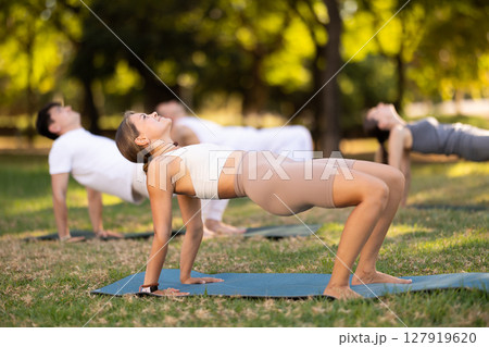 Yoga lesson visitors with girl coach perform crab pose in park Yoga lesson visitors with girl coach perform crab pose in park 127919620
