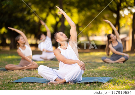 Yoga lesson visitors with guy coach perform padmasana in park 127919684