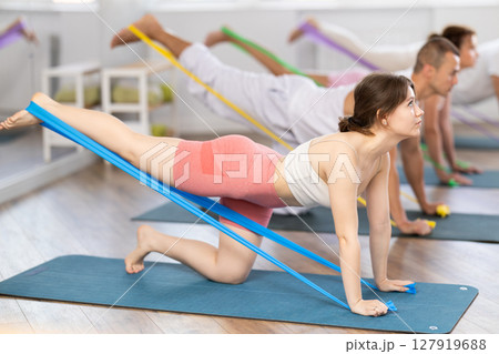 Young girl practicing back leg lift with resistance band standing on knees 127919688