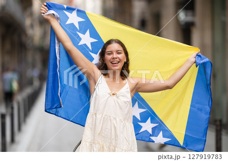 Woman waving flag of Bosnia and Herzegovina flag on street of summer European city 127919783