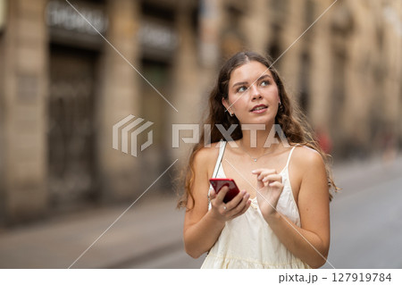 Happy young woman with mobile phone in her hands walking around city and taking pictures of sights 127919784