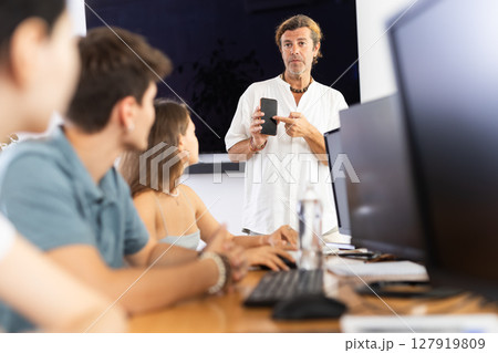 Positive teacher recommending educational mobile app to group of students 127919809