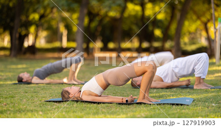 Yoga lesson visitors with coach perform Setu Badha Sarvangasana in park 127919903