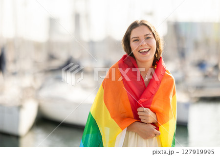 Young woman wrapped in LGBT flag at port 127919995