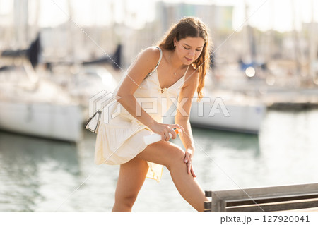 Young brunette girl applying sunscreen to her skin while walking in city 127920041