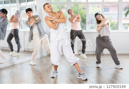 Young man standing performs basic hip hop movements in front of group of students 127920189