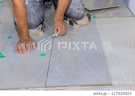 Worker meticulously places tiles on floor, ensuring precision careful alignment in renovation setting. 127920923