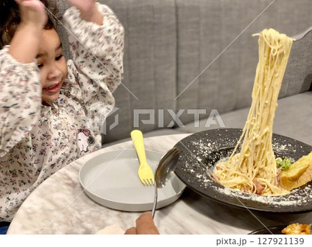 Cute little girl eating spaghetti with her mother at home on the couch Cute little girl eating spaghetti with her mother at home on the couch 127921139