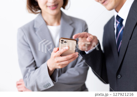 スマホを見ながら談笑するスーツを着たミドル男性ビジネスマンと女性ビジネスウーマン 127921216