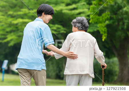杖を使うシニア女性と介護士の後ろ姿 127921508