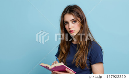 Young woman writing in notebook, looking thoughtful and engaged 127922220