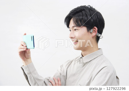 骨伝導イヤホンを付けてスマホを見る男性　20代　白背景 127922296