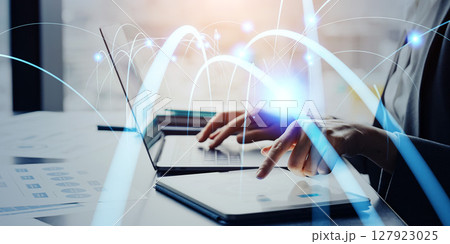 オフィスでデジタルデバイスを使うビジネスパーソンと通信ネットワークのコンセプト オフィスでデジタルデバイスを使うビジネスパーソンと通信ネットワークのコンセプト 127923025