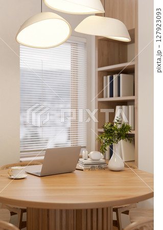 The set of a wooden round table and chairs under stylish lamps in library or study room with window. The set of a wooden round table and chairs under stylish lamps in library or study room with window. 127923093