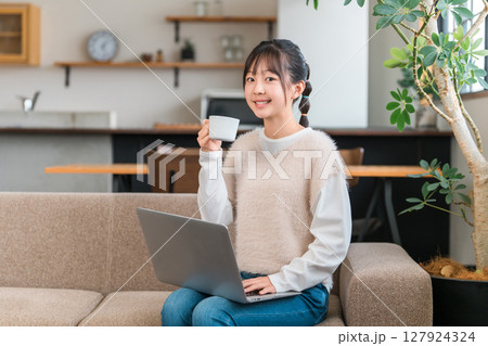 リビングのソファに座りパソコンを見ながらホットドリンクを飲む小学生,中学生の女の子 127924324