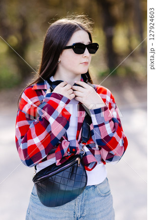 Young stylish woman adjusting headphones while listening to music outdoors 127924603