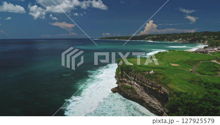 Stunning aerial view capturing a golf course on a cliff above Dreamland Beach in Bali, Indonesia, highlighting the vibrant contrast of green grass, white waves, and turquoise ocean 127925579
