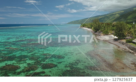 Aerial view of Tahiti island coastline showing crystal clear turquoise water gently washing a beautiful tropical beach with lush vegetation and a small white church in the background Aerial view of Tahiti island coastline showing crystal clear turquoise water gently washing a beautiful tropical beach with lush vegetation and a small white church in the background 127925637