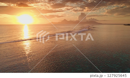 Golden sunset over the ocean illuminating a tropical island in French Polynesia, creating a breathtaking view of the coastline, waves, and the distant mountains 127925645