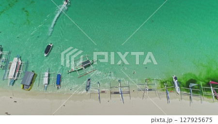 Aerial view of White Beach in Boracay, Philippines, featuring iconic paraw sailboats in turquoise waters, with a speedboat enhancing the vibrant tropical scene Aerial view of White Beach in Boracay, Philippines, featuring iconic paraw sailboats in turquoise waters, with a speedboat enhancing the vibrant tropical scene 127925675
