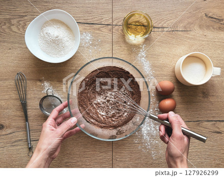 A woman prepares chocolate dough at a wooden table, top view. 127926299