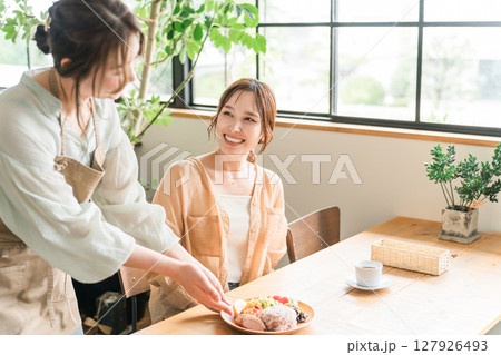 カフェでワンプレートランチを提供する店員と女性客 カフェでワンプレートランチを提供する店員と女性客 127926493