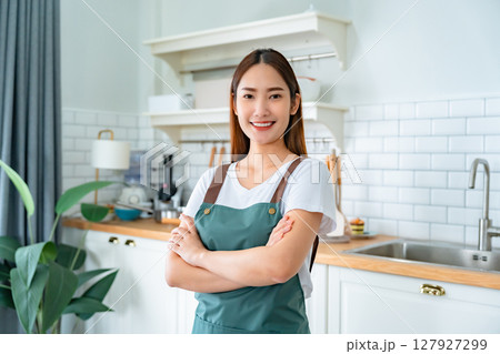 Happy young asian woman wearing apron and standing in kitchen room 127927299