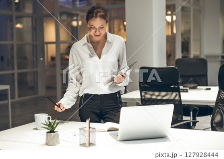 Businesswoman reviewing documents with laptop in modern office setup Businesswoman reviewing documents with laptop in modern office setup 127928444