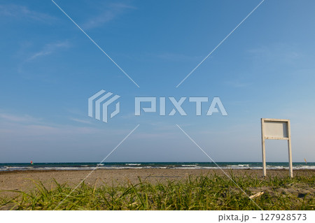 薄い雲がある真夏の青い空と木の看板が立っている芝生のあるビーチ 127928573