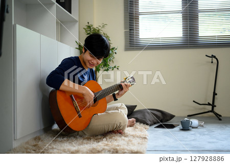 Happy asian in comfortable clothes playing guitar on the floor in a living room 127928886