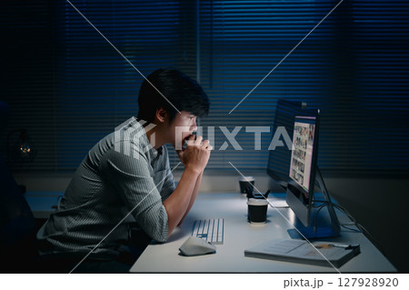 Focused businessman working late night on desktop computer in dark office Focused businessman working late night on desktop computer in dark office 127928920