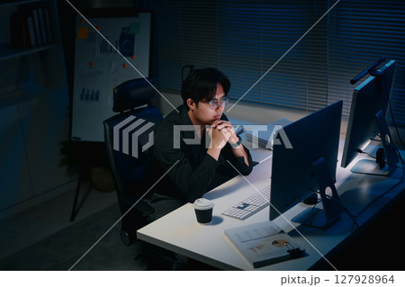 Focused businessman working late night on desktop computer in dark office Focused businessman working late night on desktop computer in dark office 127928964