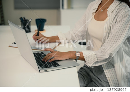 Cropped shot of young woman working at a desk with a laptop and notebook Cropped shot of young woman working at a desk with a laptop and notebook 127928965