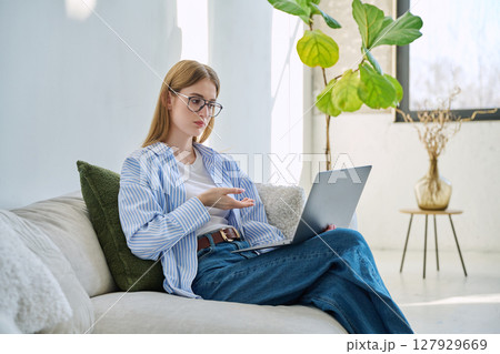 Young teenage girl using laptop for video chat sitting on sofa at home Young teenage girl using laptop for video chat sitting on sofa at home 127929669