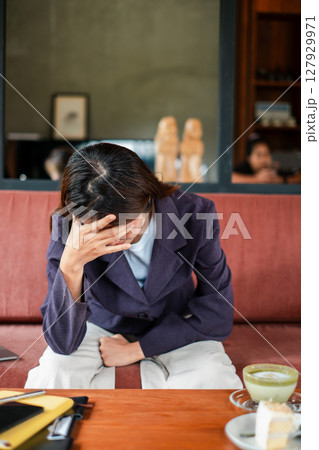Woman in a cafe looking stressed, sitting with hand on forehead, reflecting in a cozy setting. Woman in a cafe looking stressed, sitting with hand on forehead, reflecting in a cozy setting. 127929971