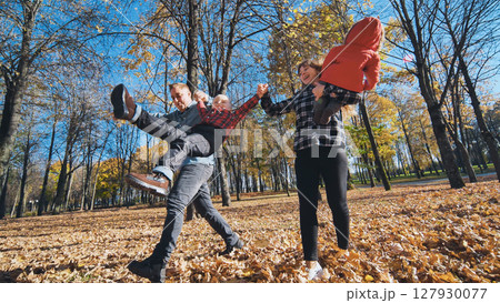 Parents lifting, playing with children among autumn foliage in sunlit park setting Parents lifting, playing with children among autumn foliage in sunlit park setting 127930077