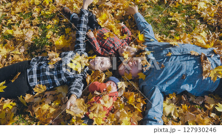 Family enjoying a beautiful fall day, lying on vibrant, colorful leaves in a park, embracing togetherness and the joy of nature 127930246