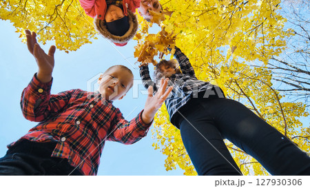 Family enjoying autumn park, holding yellow maple leaves from low perspective 127930306